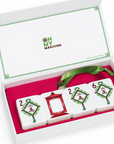 An ornament of four white Chinese mahjong tiles displayed inside an open white gift box with a pink interior and green ribbon. The lid shows the brand name 'Oh My Mahjong'.