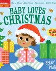 Front cover of the children's board book 'Baby Loves Christmas' by Becky Paige, featuring a cartoon baby in a Santa hat holding a gift box, surrounded by Christmas trees, wrapped presents, and candy canes on a light blue background.