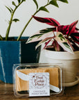 A plastic-wrapped square of chocolate peanut butter fudge on a wooden surface with a plant in the background.