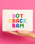 White pouch with colorful text 'DOT CRACK BAM' held by a hand against a pink background