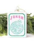 Christmas ornament with 'Joker' text and design, hanging against a white background with greenery.