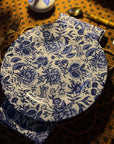 A blue and white floral patterned melamine dinner plate on a table setting with cutlery and a orange patterned tablecloth.