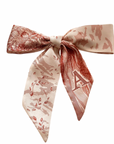 A pink and beige silk scarf with a floral pattern and a bow tie.