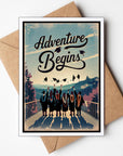 Greeting card with graduates and 'Adventure Begins' text on a scenic background, placed on a brown envelope.