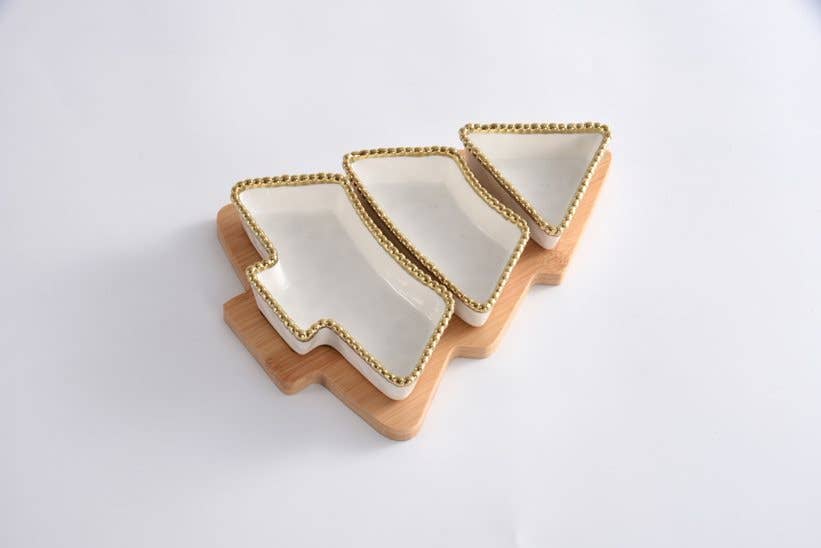 Set of four white ceramic trays with gold rims on a wooden stand against a white background