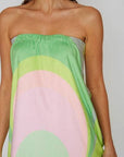 Woman wearing a towel wrap with green and pink abstract pattern on a plain background