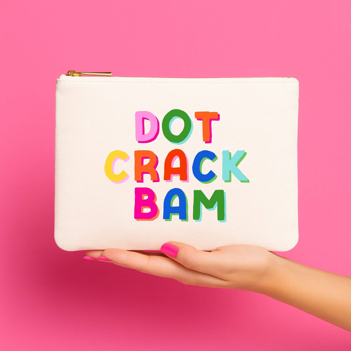 White pouch with colorful text 'DOT CRACK BAM' held by a hand against a pink background