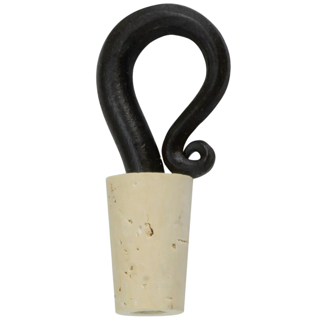 A black, hand-forged steel bottle stopper with a swirling handle design, placed in a beige cylindrical holder.