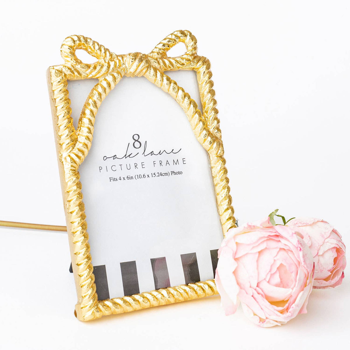 Gold picture frame with a decorative bow design on a white background with a pink rose.