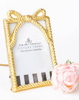 Gold picture frame with a decorative bow design on a white background with a pink rose.