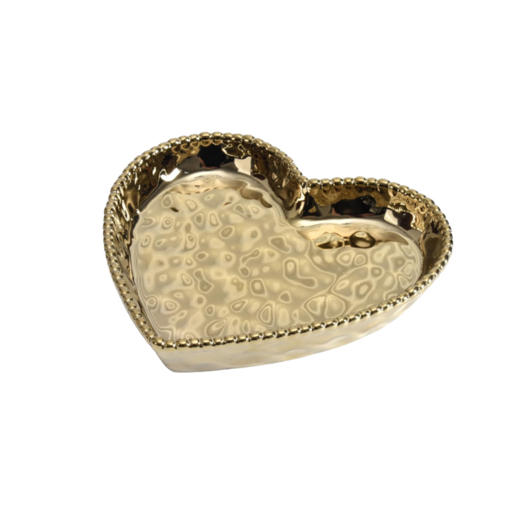 A gold-colored heart-shaped dish with intricate patterns inside the bowl and a beaded edge.