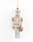 A frosted glass Christmas nutcracker ornament with gold and silver accents, hanging from a gold string against a plain white background.
