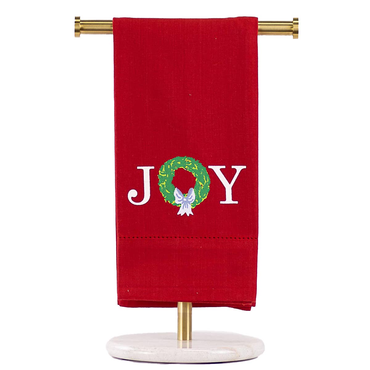 A red kitchen towel hanging from a gold stand with a white marble base, featuring the word 'JOY' embroidered in white with a green wreath and white bow.