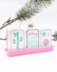 Decorative mahjong ornament with pink stand and card designs on a white background