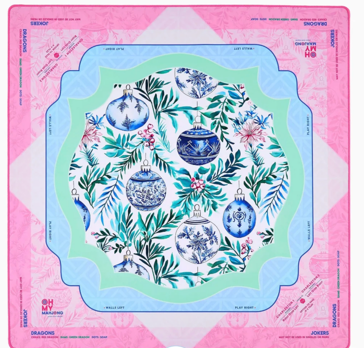 A Mahjong mat featuring a festive Christmas design with blue and white ornaments, green foliage, and pink flowers, framed by a pink and light blue border with brand text.