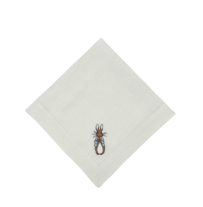 A white linen napkin with a small piece of embroidered fabric featuring a rabbit design, likely intended for an Easter-themed setting.