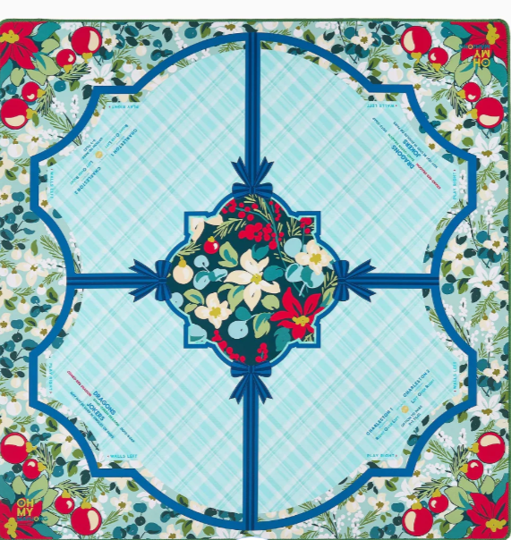 A square decorative textile or mat with a festive holiday floral pattern. The design features a central light blue plaid arch with a dark blue border, a central floral wreath motif in red, green, and cream, and a border of poinsettias and white flowers with small blue text details.